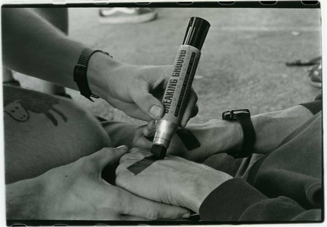 Two persons mark each others hands with big 'x's in black marker to signify they are Straight Edge